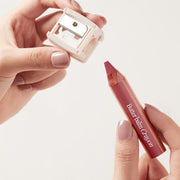 ProtoClinical k-beauty CLIO Butter Balm Crayon + Sharpener Set 3.9g (9colors) lineup of nine lip-and-cheek crayon pencils in nude, rose, and berry tones on a light tabletop