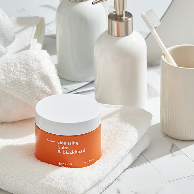 ProtoClinical k-beauty Hanskin Cleansing Balm & Blackhead 80g round brown cleansing balm jar near the lower left on a warm gray background with pale beige highlights.