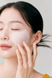 ProtoClinical k-beauty celimax Pore+ Dark Spot Brightening Pad 100ml/40ea translucent round pad applied to a model's cheek with fingers against a soft gray background