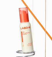 ProtoClinical k-beauty LABO-H Hair Strengthening Essence 75ml as an ivory essence bottle with a translucent coral cap leaning on a chrome ring against a white background with an orange diagonal line