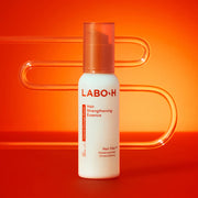 ProtoClinical k-beauty LABO-H Hair Strengthening Essence 75ml as a single upright ivory essence bottle with a translucent coral cap on a vivid orange background
