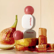 ProtoClinical k-beauty lilybyred Sugar Wrapping Tint Gloss 6g (8colors) rounded lip gloss bottle with a glossy pink bulb cap, doe-foot applicator, and a circular red-pink swatch on a white background