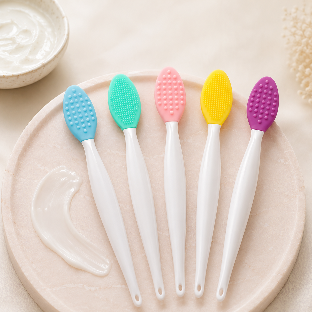 Five colorful silicone skincare applicators arranged on a blush stone tray